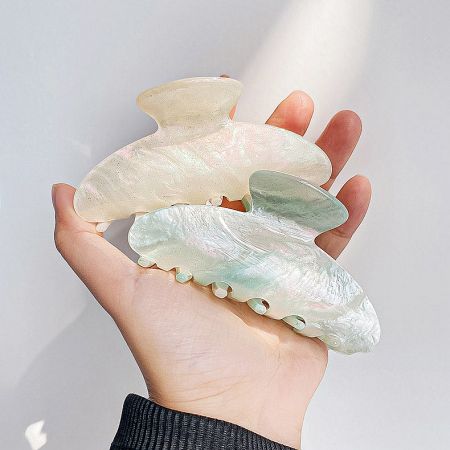 A hand holding two pearlescent hair clips to show their size and design.