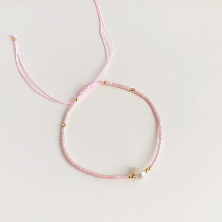 A charming pink beaded bracelet with gold details and a central pearl, perfect for stacking.