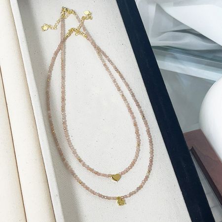 Pink beaded necklace with silver heart charm presented in a jewelry box.