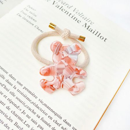 Detailed view of a single pink and white marbled acetate bear charm on a beige elastic hair tie.