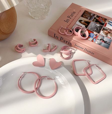Pink enamel earrings artfully arranged next to a book about Paris, evoking a chic and fashionable vibe.