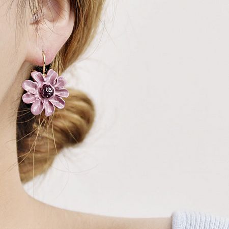 Close-up of the flower-shaped earring being worn, showing its scale and detail.