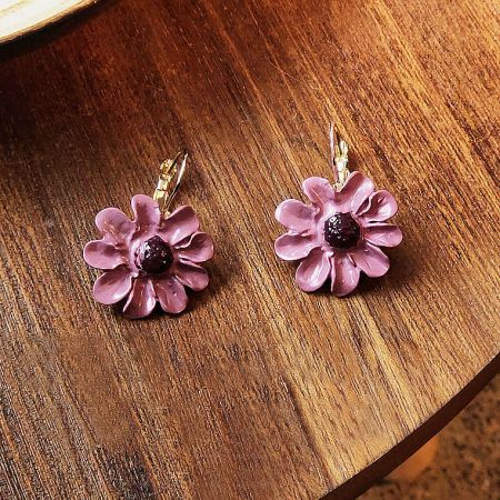 The pink flower earrings displayed on a rustic wooden table to highlight their craftsmanship.