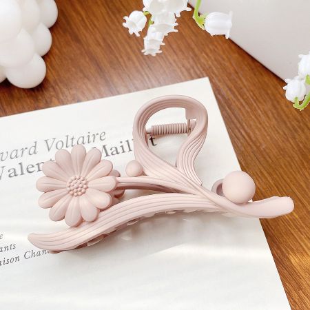 Close-up of a delicate pink daisy flower hair claw clip against a white background.