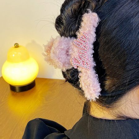 A cute pink fuzzy hair clip featuring the word 'kiss' in a playful font.