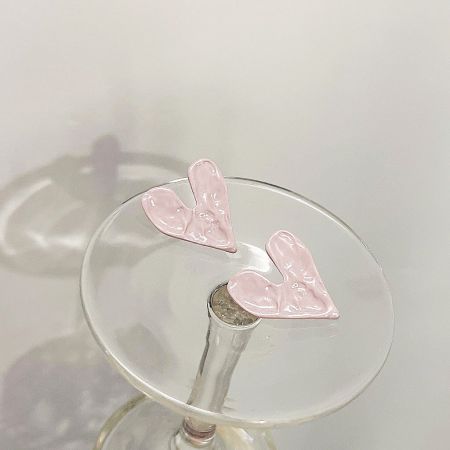 A creative lifestyle shot of the pink heart earrings resting on the rim of a martini glass.