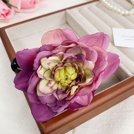 Close-up of a vibrant pink and purple artificial flower hairclip in a presentation box.