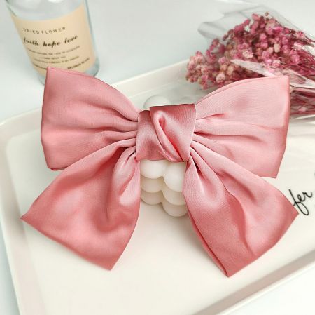 A lovely pink satin bow hair clip displayed in a lifestyle setting.