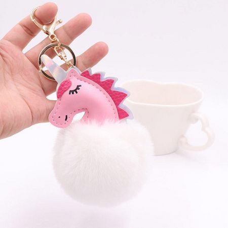 Close-up of a pink PU leather unicorn keychain with a soft white pom-pom fur ball.