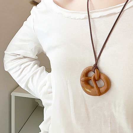 A model wearing the realistic pretzel-shaped PU pendant necklace against a white shirt.