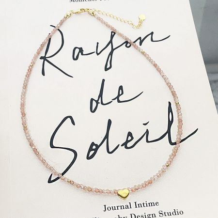 Pink beaded necklace with heart charm on a branded display card.