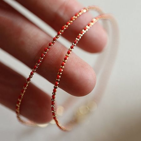 A hand holding the red and gold braided cord bracelets, showing the fine details.