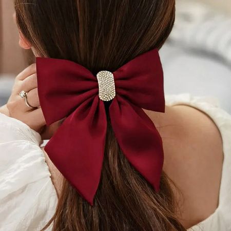 Detailed view of the red bowknot hair clip with a sparkling gold and rhinestone centerpiece.