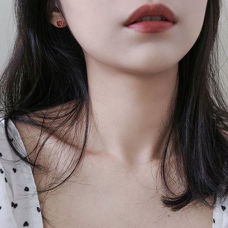 A pair of red heart stud earrings displayed on a white card.