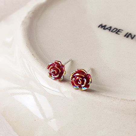 Lifestyle product shot of the 3D red rose earrings with iridescent details resting on a white ceramic plate.