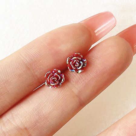 Detailed view of the red resin rose stud earrings with gold accents held between fingers to show craftsmanship.