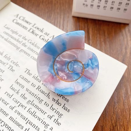A close-up of a single pastel-colored conch shell hair clip resting on a book.