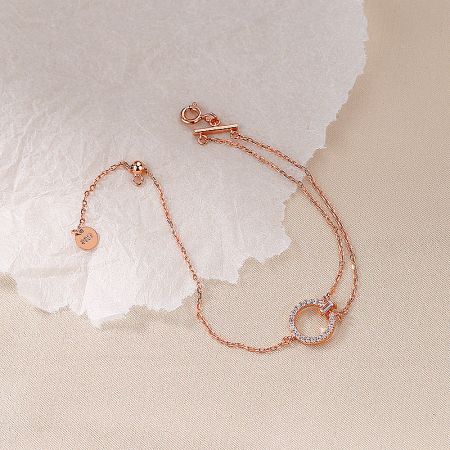 Elegant rose gold version of the asymmetric chain bracelet with a zircon-encrusted circular pendant.