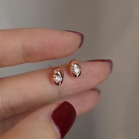 A hand with red nail polish holding the elegant gold bean-shaped stud earrings.