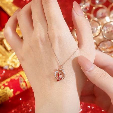 A close-up of a rose gold necklace featuring a circular pendant with red and clear gemstones.