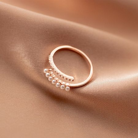 The rose gold finish of the delicate zircon and pearl adjustable ring, worn on a finger.