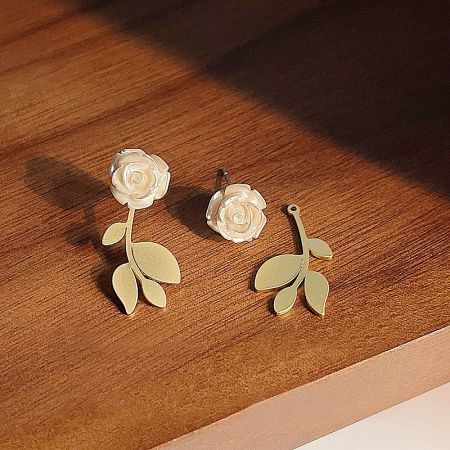 A creative shot showing one complete white rose earring next to its gold-plated base and leaves.