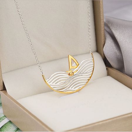 Luxury presentation of the sailboat pendant necklace, highlighting its dual-tone finish.