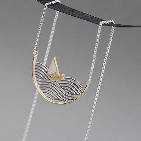 Close-up view of the movable wave and sailboat pendant in gold and silver tones.