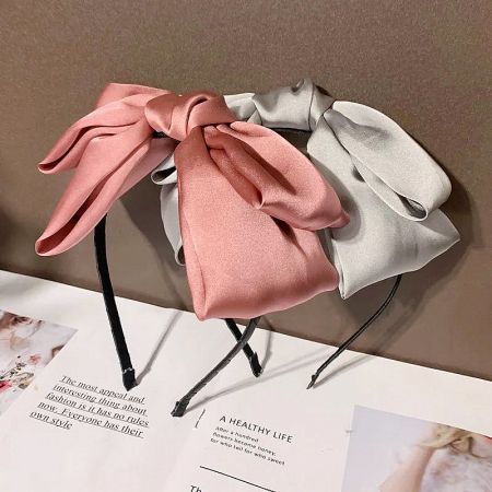 Close-up of two satin headbands with large bows, one in pink and one in a darker shade.