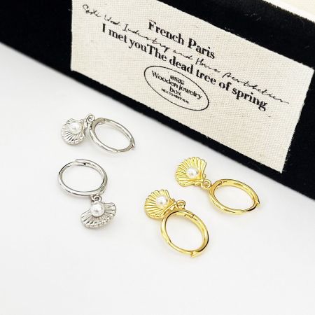 Both gold and silver pearl shell earrings elegantly displayed next to a wooden jewelry box.