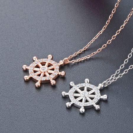 A pair of ship's wheel pendants in rose gold and silver, both adorned with clear, sparkling stones, displayed side-by-side.
