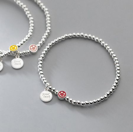 Close-up view of two sterling silver beaded bracelets, one featuring a yellow smiley face charm.