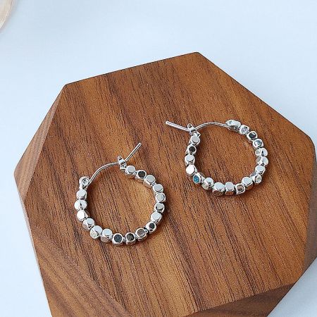 Detailed view of the silver hoop earrings with beaded texture on a wooden block.