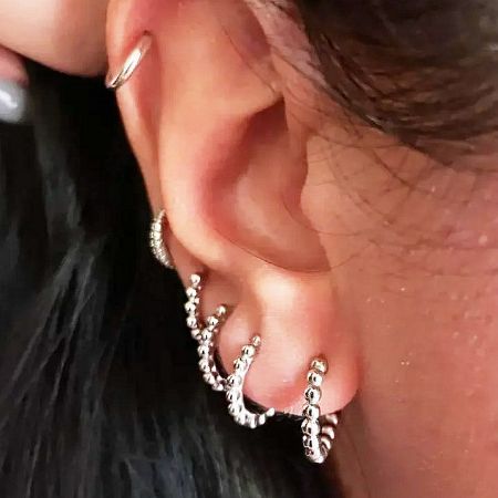 A model showcasing multiple silver beaded hoop earrings in different ear piercings.
