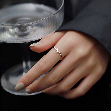 A woman's hand wearing a delicate silver ring shaped like a bird in flight.