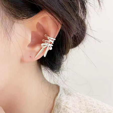 Close-up shot of the matte silver bow ear cuff on a model's ear.