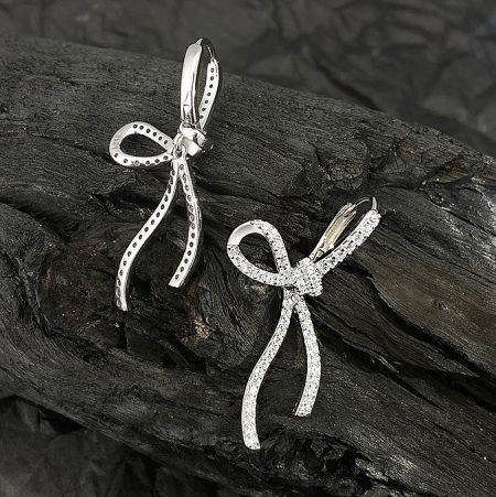 Product shot of the 925 sterling silver bow earrings on a dark wood surface.