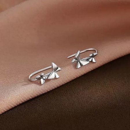 A pair of sterling silver bow-shaped hook earrings from the creative design set, shown on a textured surface.