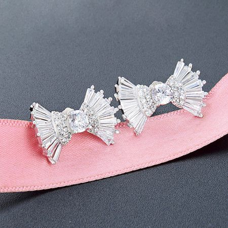 The silver bow earrings with clear gemstones elegantly presented on a pink ribbon.