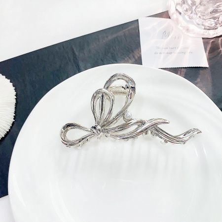 Close-up of the silver metal ribbon hair clip with a central pearl accent on a white plate.