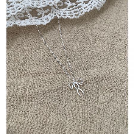 Detailed shot of the silver bow pendant on a textured fabric, showing its fine craftsmanship.