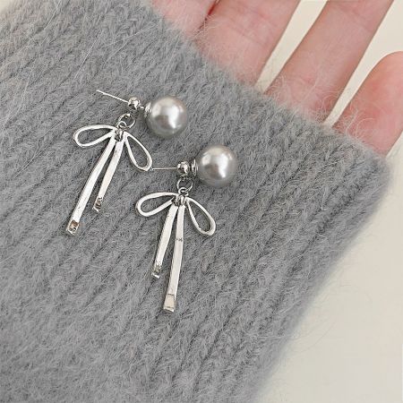 Silver Plated Grey Color Pearl Bowknot Drop Earrings (5 Pairs) - A pair of silver-plated drop earrings with grey pearl studs and delicate bowknot charms with long tassels, displayed on a textured grey surface.