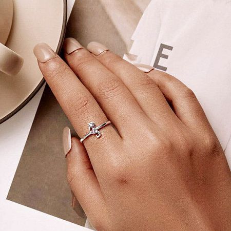 A delicate silver bow-shaped ring with a central gemstone, worn on a woman's finger.