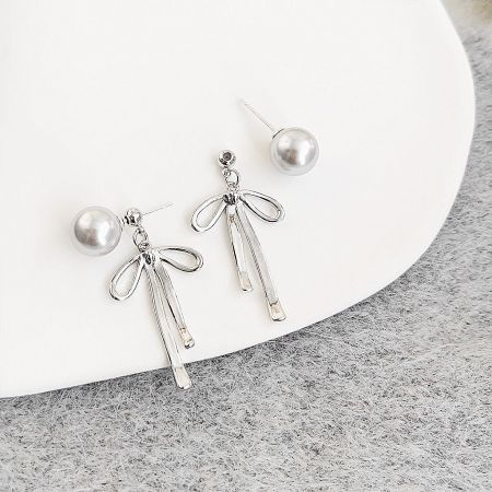 Full view of the silver bow tassel earrings against a grey background.