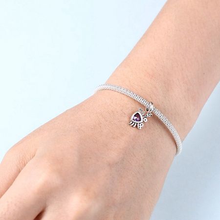 Close-up view of the purple crab charm on a silver bracelet worn on a wrist.