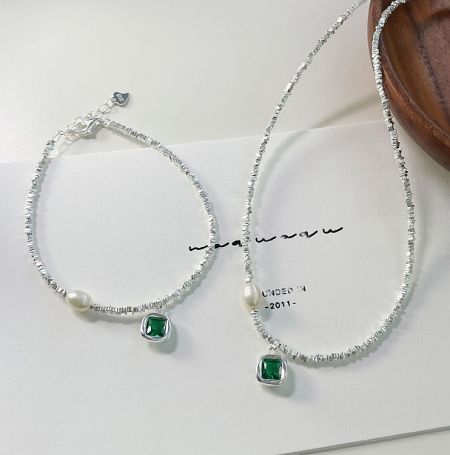A pair of 925 Sterling Silver Pearl Emerald Bracelets displayed on a white surface, highlighting the intricate details of the green gemstones and pearls.