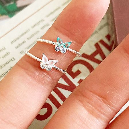 Close-up of two sterling silver butterfly rings with white and blue gemstones.