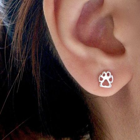 Close-up of a sterling silver paw print stud earring being worn.
