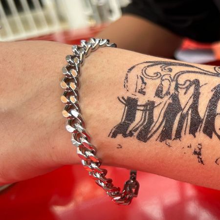 Men's Cuban chain bracelet worn on a tattooed wrist, highlighting its stylish look.