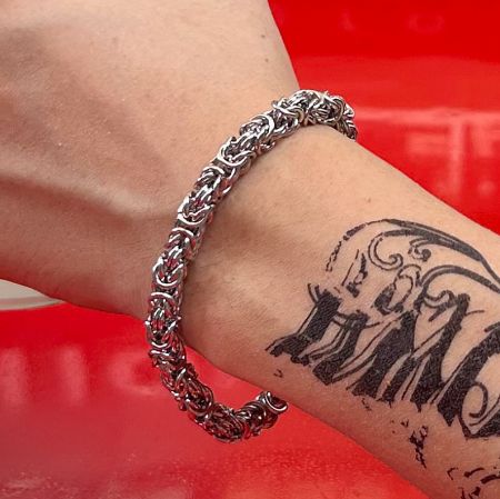 A man wearing the braided stainless steel bracelet on his tattooed wrist.
